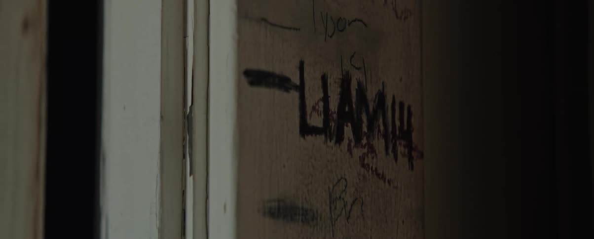 A black writing on a wooden wall with a black shadow passing over the writing