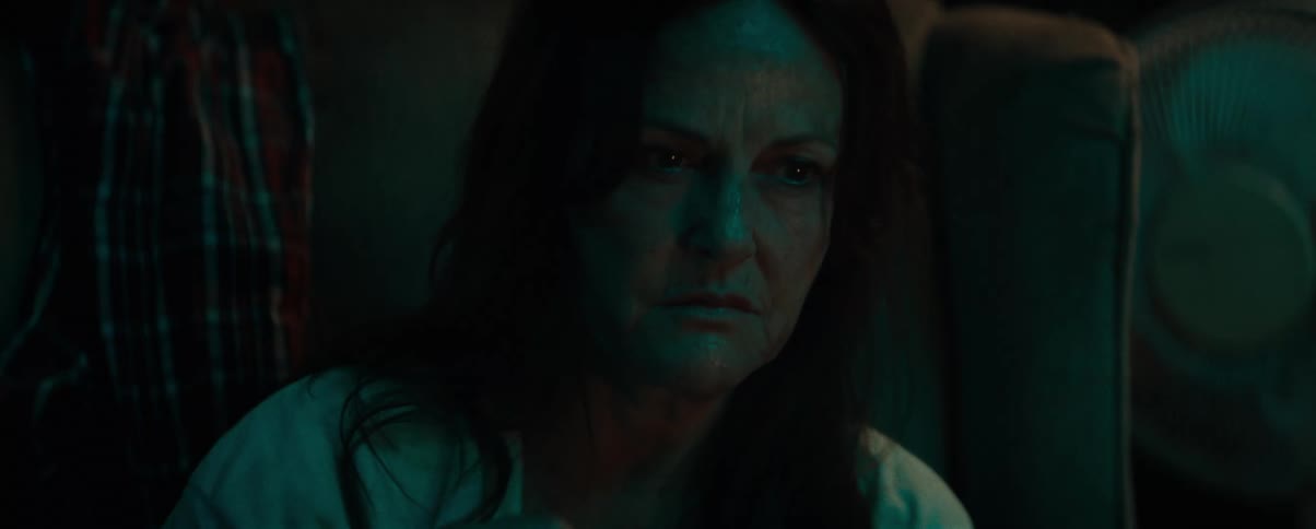 A sad woman holding a bowl sits on a couch in a dimly lit room at home