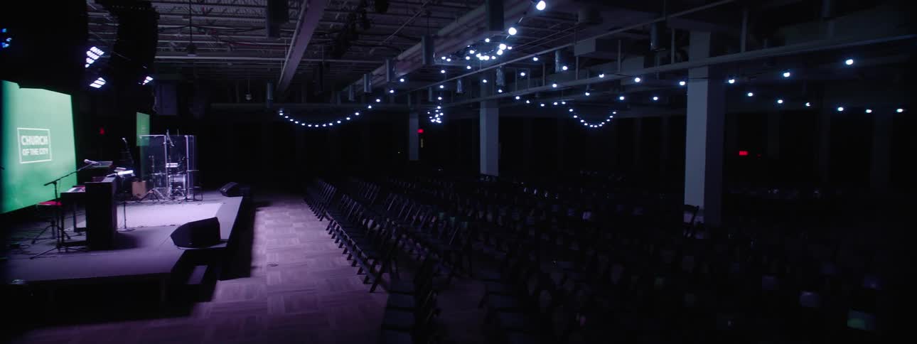 Interior of a dark auditorium with a stage with a screen and lighting