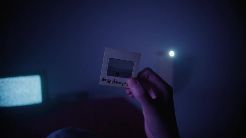 A hand holding a vintage slide with a pink and blue light near a television screen showing static