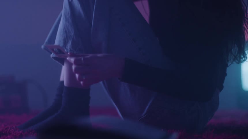 A person sitting on a bed picking up a square object and then dropping it