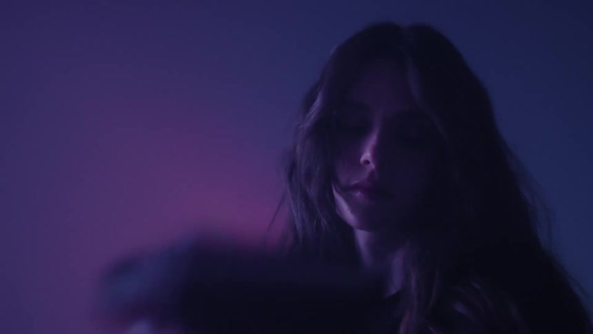 A young woman with long hair in a dimly lit room bathed in blue lights holding a vintage film camera