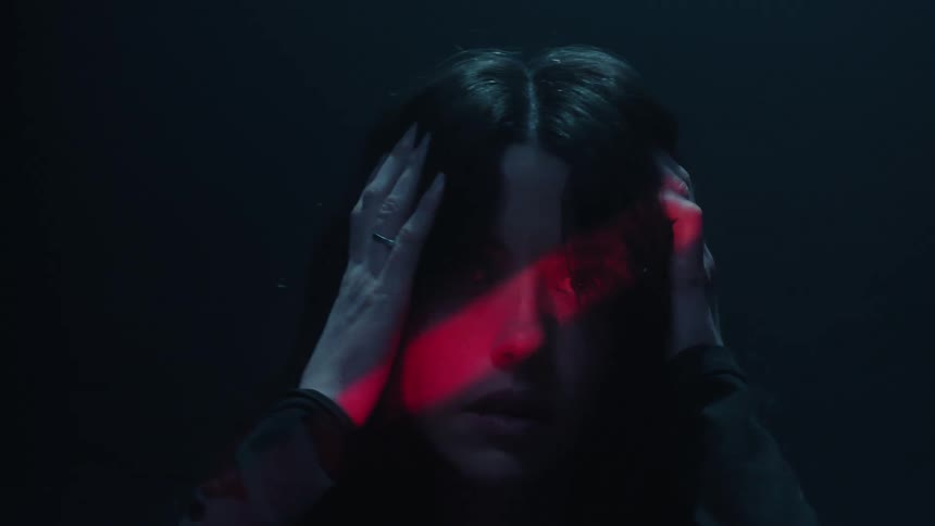 A woman rubs her hair and head while a red light shines in her face