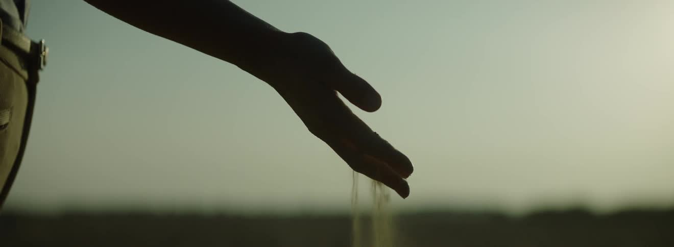 Sand sifting through fingers from silhouette of a hand at dusk