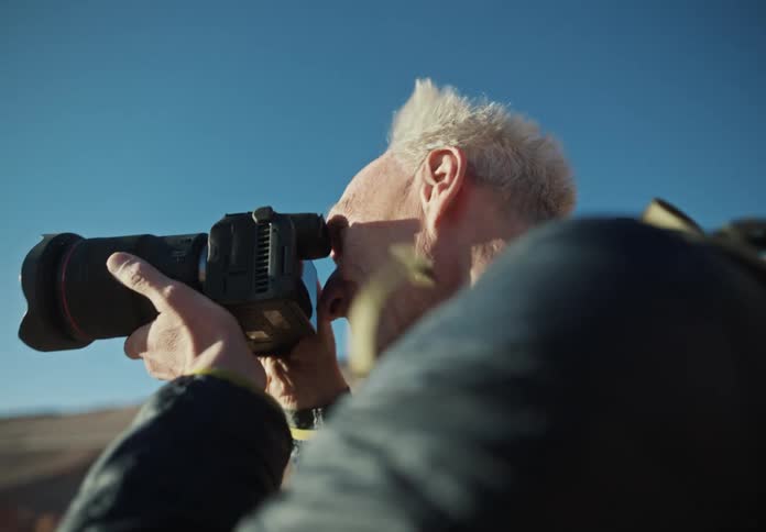 An elderly man out in nature lifts his camera to take photos