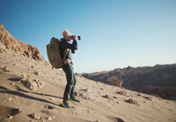 Man with a backpack and a professional camera photographing and hiking in a desert mountain