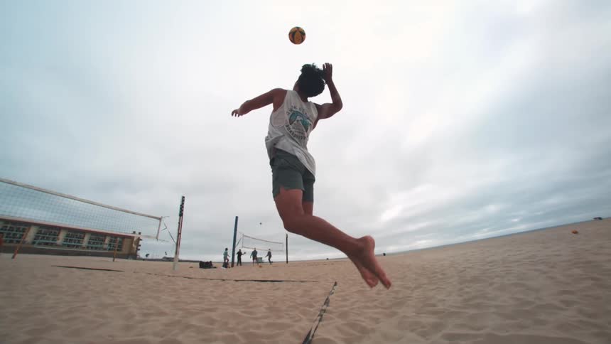Man jumps to serve the volleyball during a game on the beach