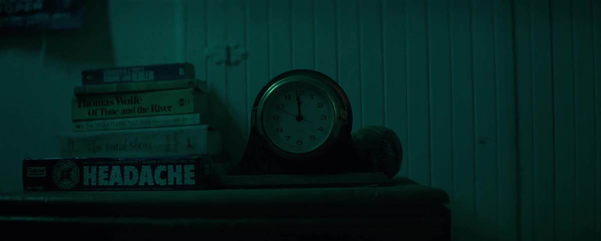 An antique clock on a shelf with books in a dark environment
