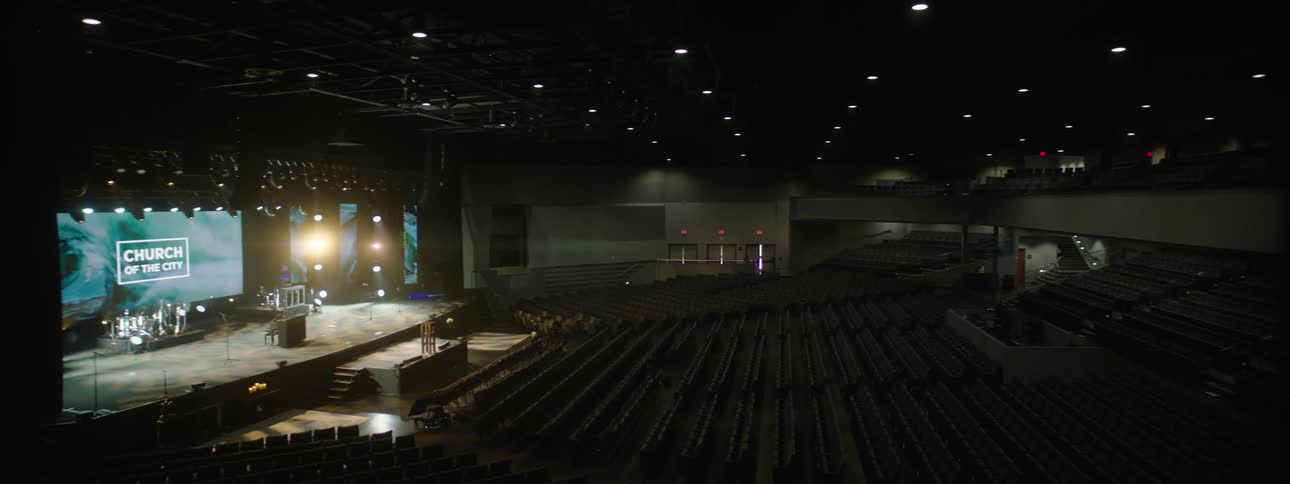 Interior architecture of an auditorium with organized chairs and a stage lit with a large screen