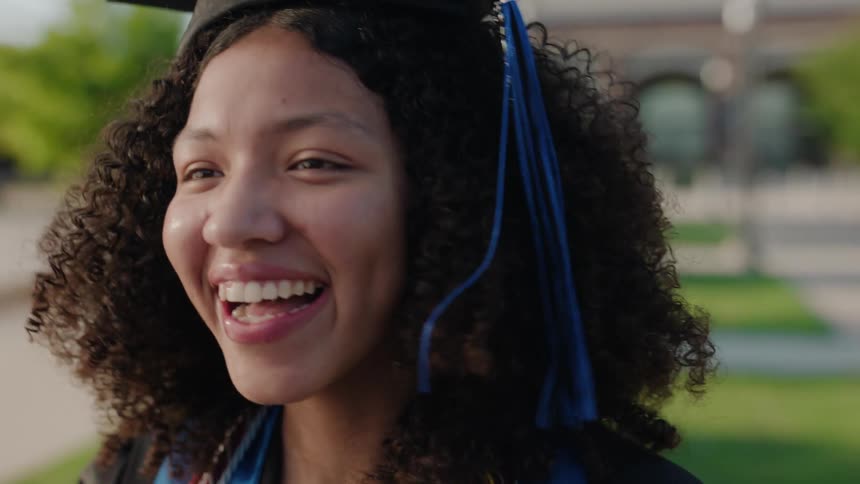 A closeup of a happy teen woman wearing a graduation cap with a blue tassel