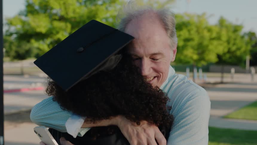 Two people hugging each other one in a graduation gown and the other with gray hair celebrating a moment
