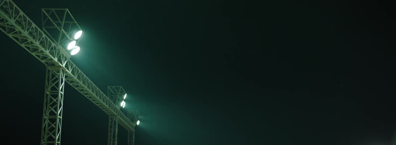 A row of bright stadium lights mounted on a tall metal structure against a dark evening sky