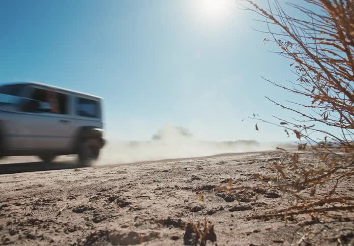 White jeep driving across the desert on a dirt trail leaving a dust cloud behind