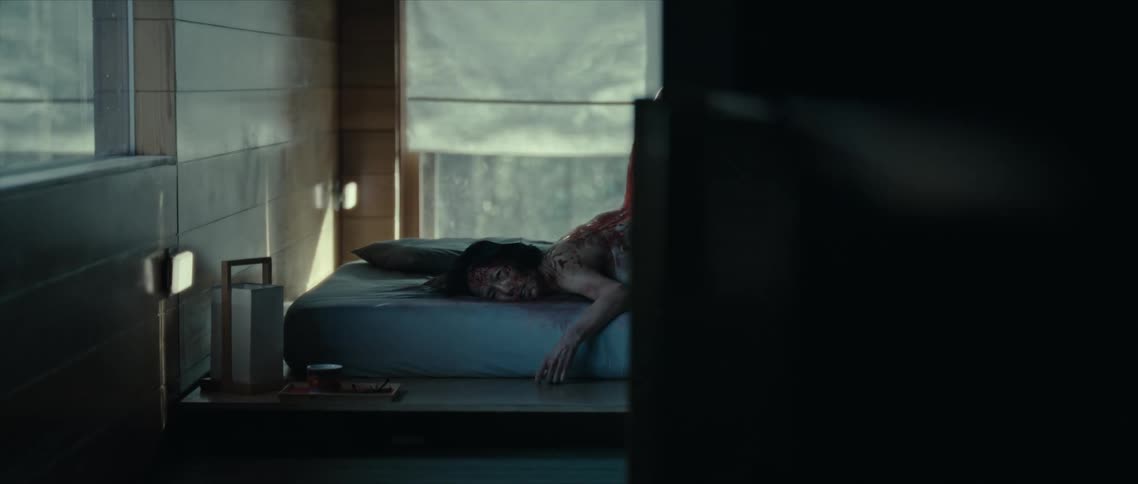 Woman grimaces while lying on the bed in front of a window