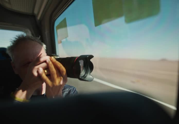 Man inside a moving van taking photos of a natural desert landscape