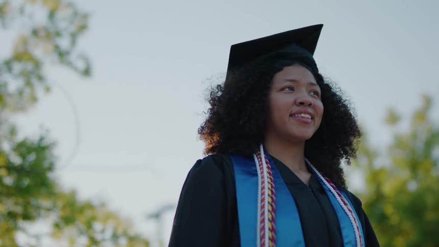 Woman smiles while wearing her graduation cap and gown