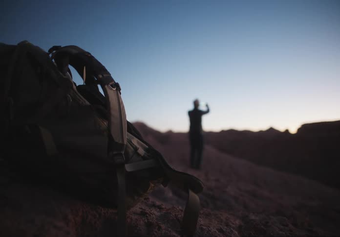Backpacking on the rock of a desert mountain and the silhouette of a person in the blurred background
