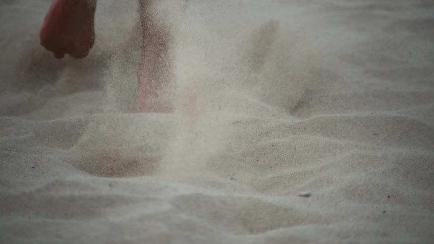 A closeup view of a persons bare feet running on sandy ground
