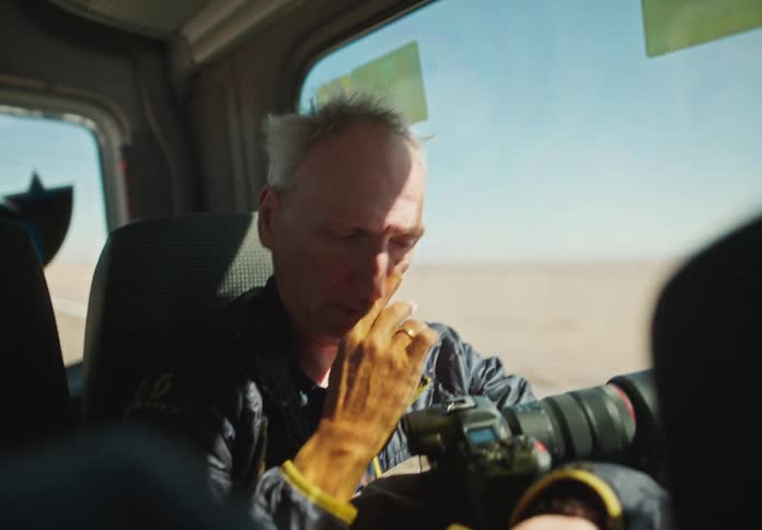 An elderly man holding a camera pointed at a glass window of a moving vehicle