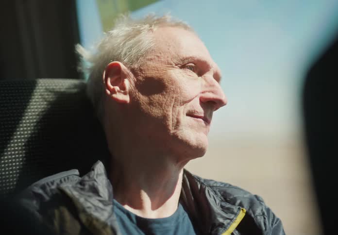 An elderly man wearing a coat enjoys traveling on a train
