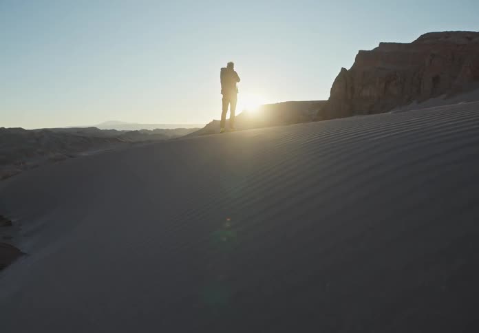 A person walking on the sand of a desert and the sun is shining brightly in the sky