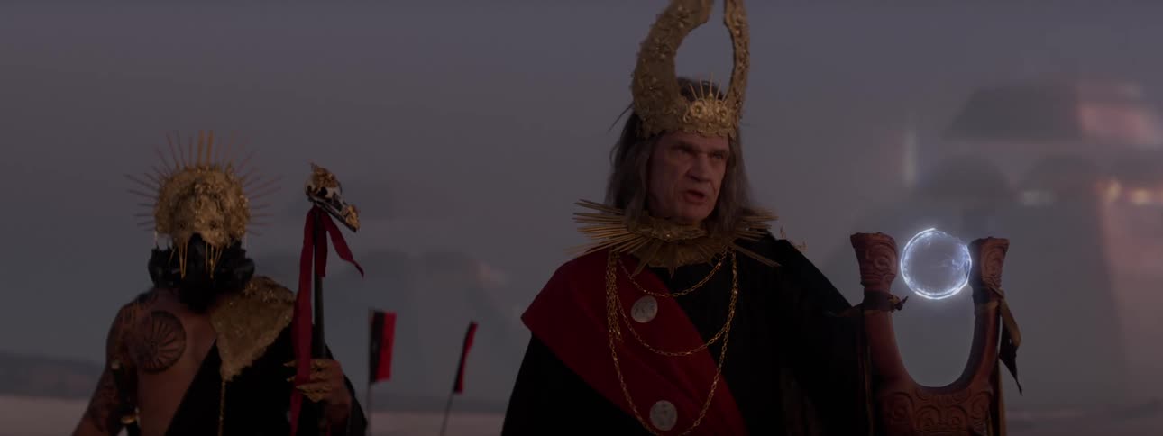 Two individuals in elaborate costumes with helmets one of which has a helmet with prominent horns holding a magical staff and talking