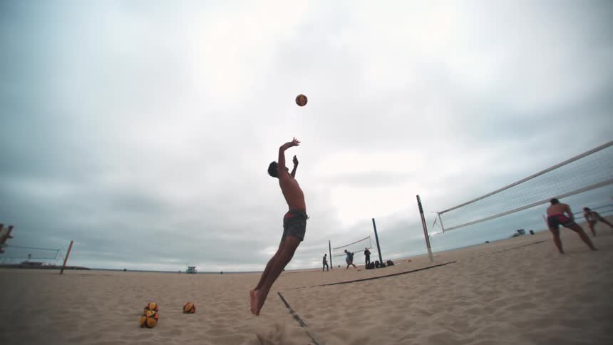 A man palms a volleyball on a beach volleyball court