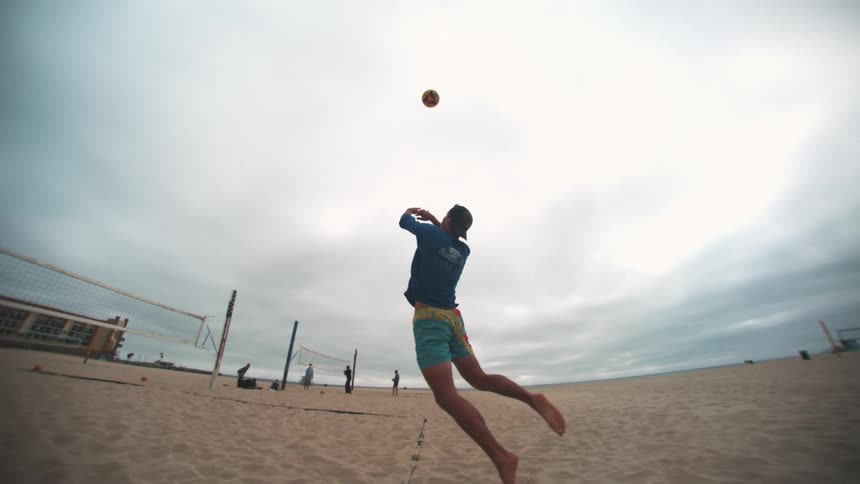 Man jumping and throwing a shot while playing volleyball on the beach sand