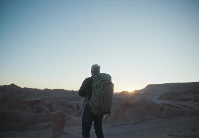 Man with a backpack watching the sunset in a desert terrain with rock formations