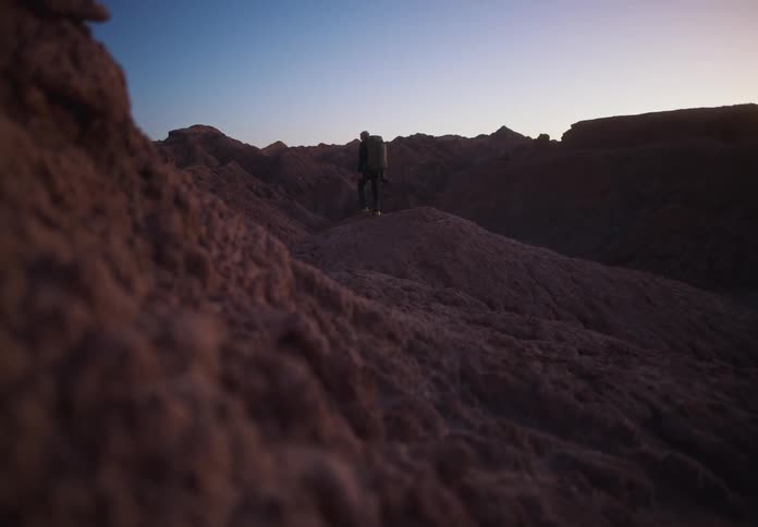 Man walking through rocky and desert mountains at sunset