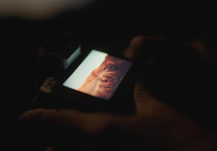A persons hands that are holding a digital camera with photos of landscapes playing on the screen