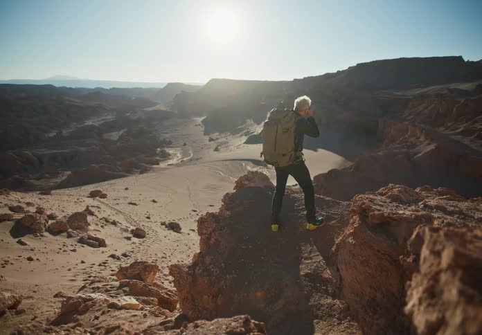 Man with a professional camera on top of a rock in a desert environment taking photos
