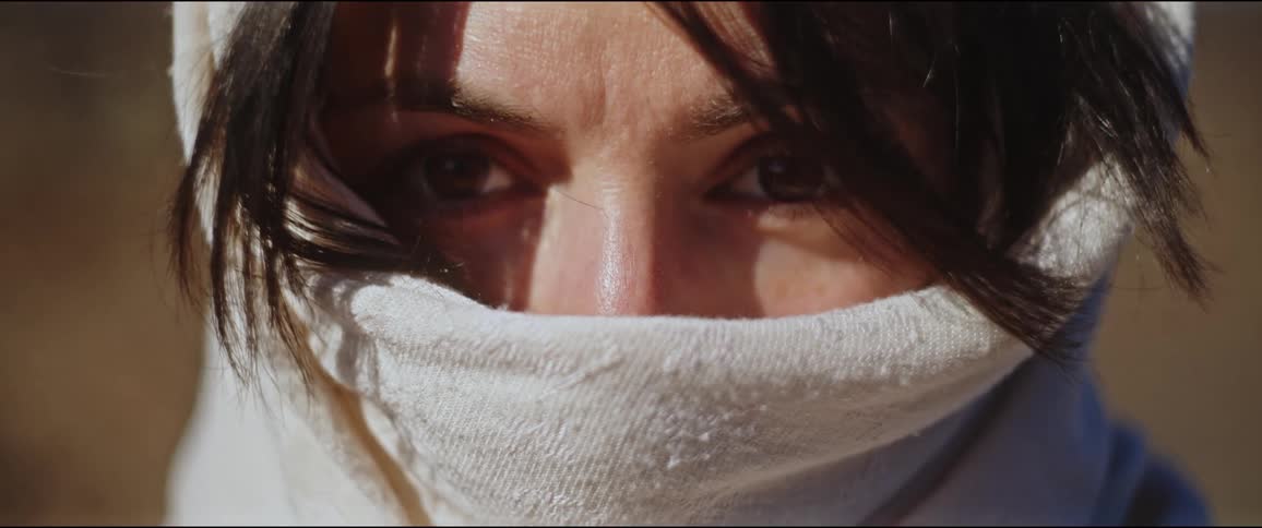 Closeup on the face of a woman with black hair and using a white scarf on her face