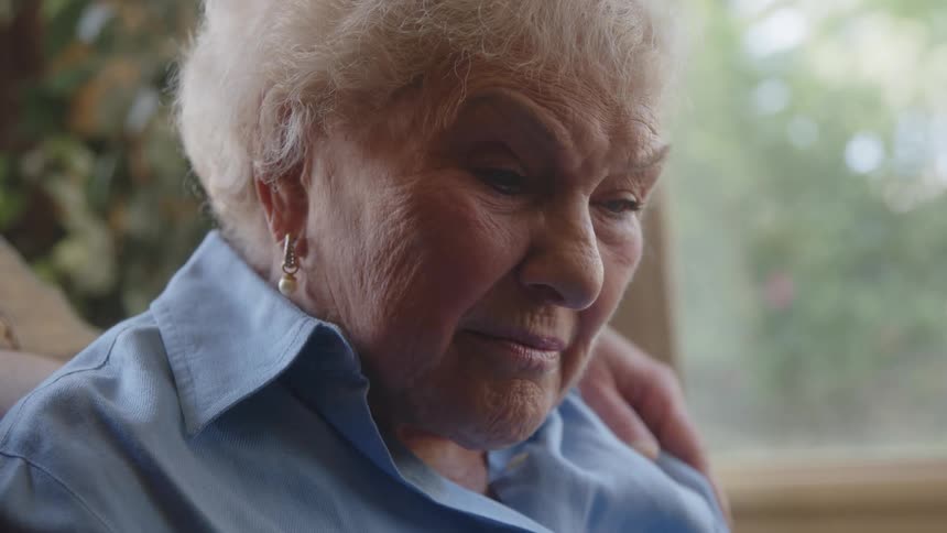 Elderly couple talk to each other in front of a window overlooking trees