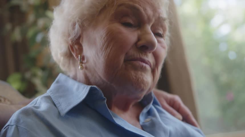 Close up of the face of an elderly woman talking to someone sitting next to her