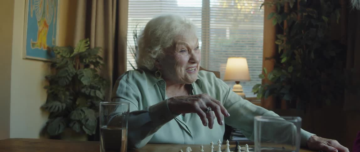 Two elderly people sitting at a table with chess talking smiling