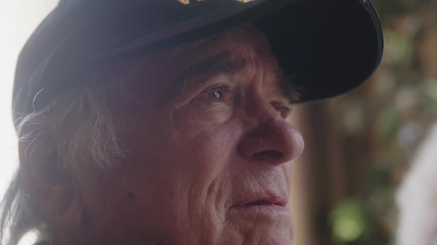 Side portrait of an elderly man wearing a black cap talking