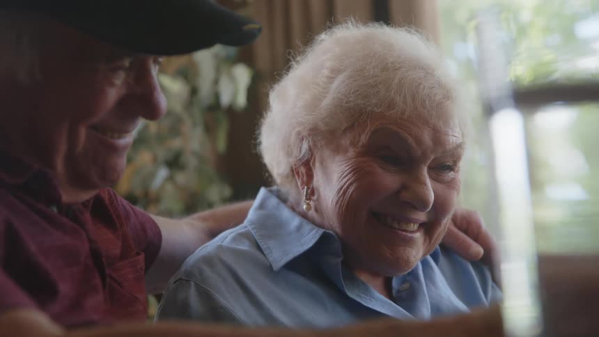 An elderly couple talk and hug while looking at something