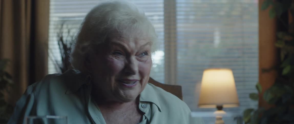 An elderly white woman sitting in a chair in a room and laughing and talking