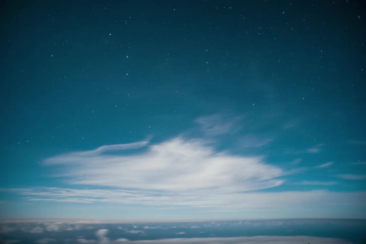 Starry night sky above a layer of clouds with the day dawning and changing tones