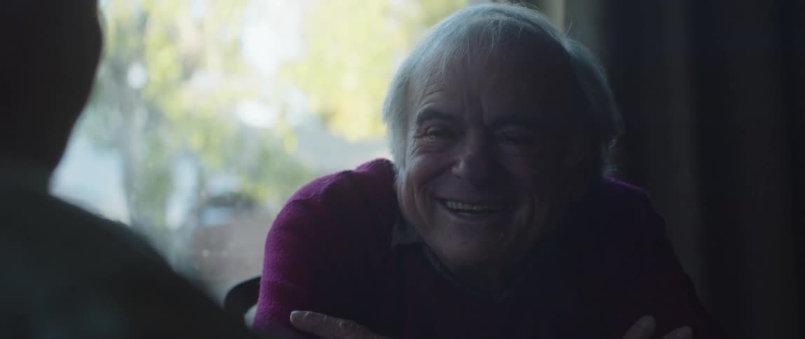 An elderly smiles and laughs while having a conversation at home
