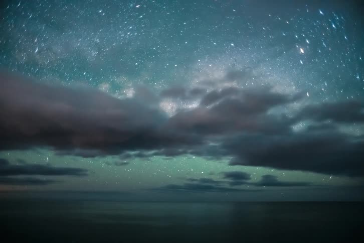 Natural scenery of an expansive ocean against a starry sky with clouds passing by