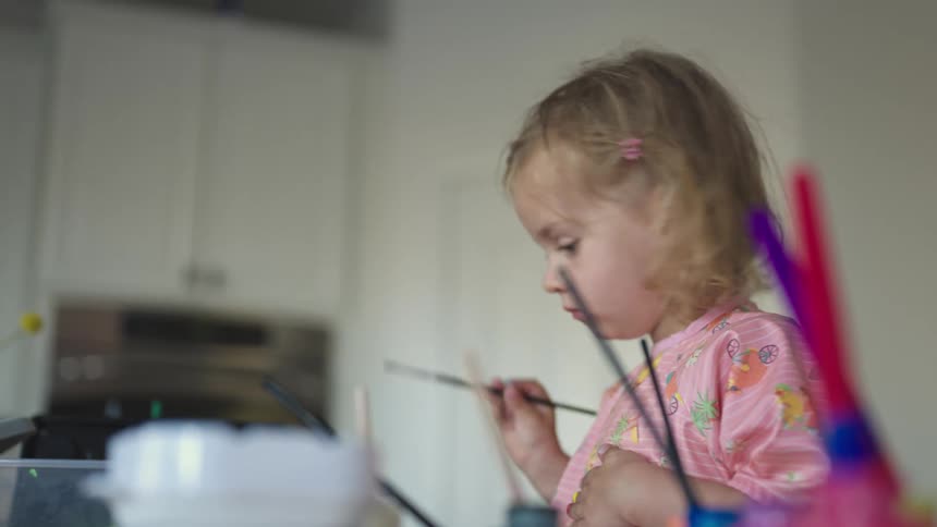 A girl wearing pink clothes painting with watercolors at home