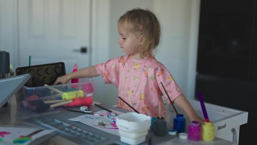 Little girl taking a tube of green paint from a box