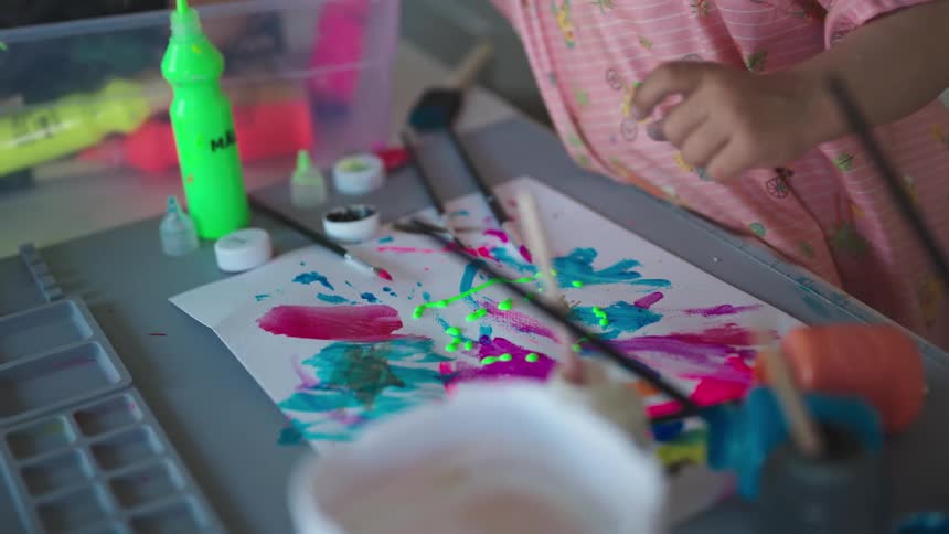 Little blonde girl playing paint on a white sheet