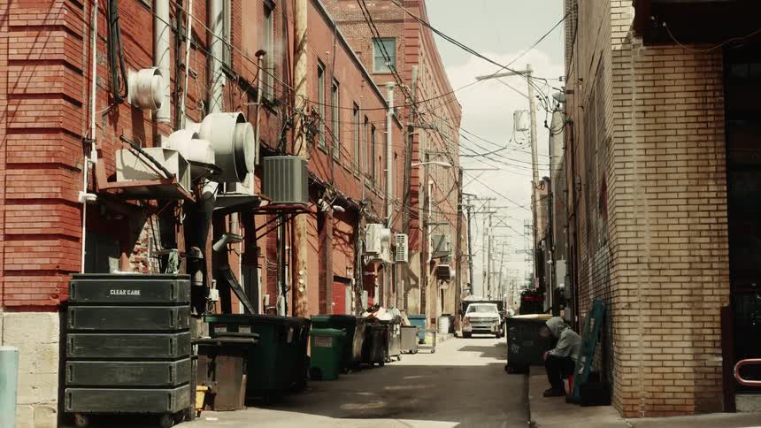 Alley in a residential street with cables and lampposts and a person sitting on the side