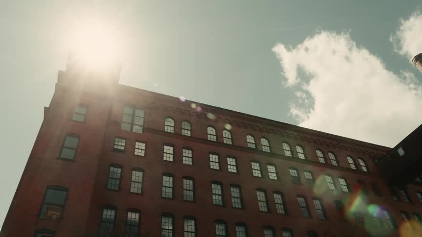 The sun shines over a large brick building viewed at an angle from below