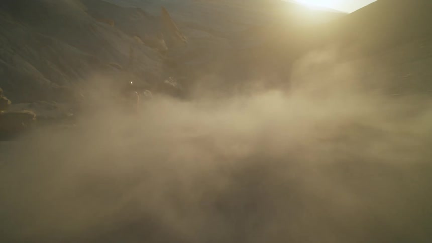 A person riding a bicycle down a dusty slope with the sun low on the horizon