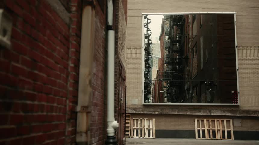 Large mirror hanging in an alley reflects apartment buildings with fire escapes
