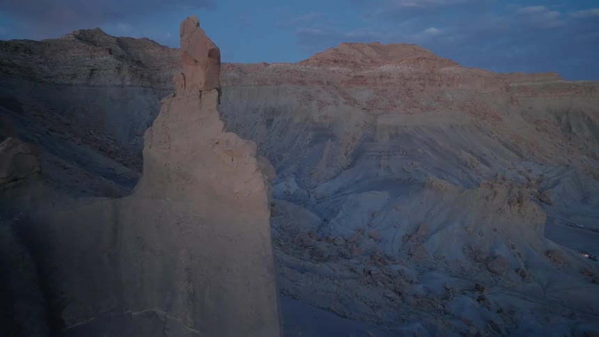 Rock formation sits on mountain slope towering over arid valley after dusk on a cloudy day